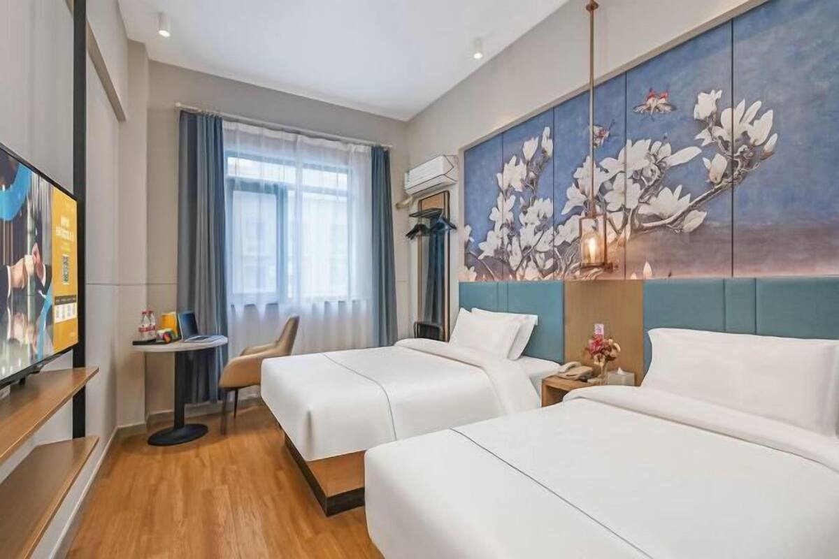 A hotel room with two beds, a television, a small table, and a painting on the wall.