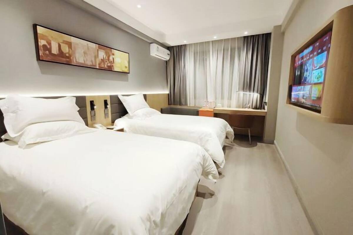 A hotel room with two beds, a desk, a TV, and a painting on the wall.
