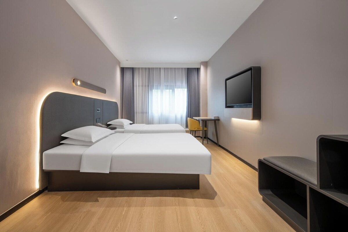 A hotel room with two beds, a flat-screen TV mounted on the wall, and a small table with a chair.