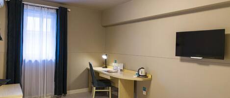 Una camera d'albergo con un letto, una scrivania con una sedia, una televisione e una finestra con tende.