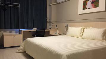 A hotel room with a bed, desk, chair, and an air conditioning unit.