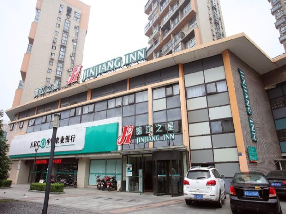 A building with a prominent 'JINJIANG INN' sign, a storefront with a green awning, and several parked cars in front.