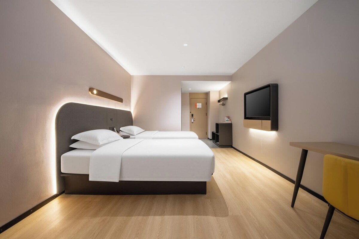 A modern hotel room with a large bed, bedside tables, a flat-screen TV, and a small desk.