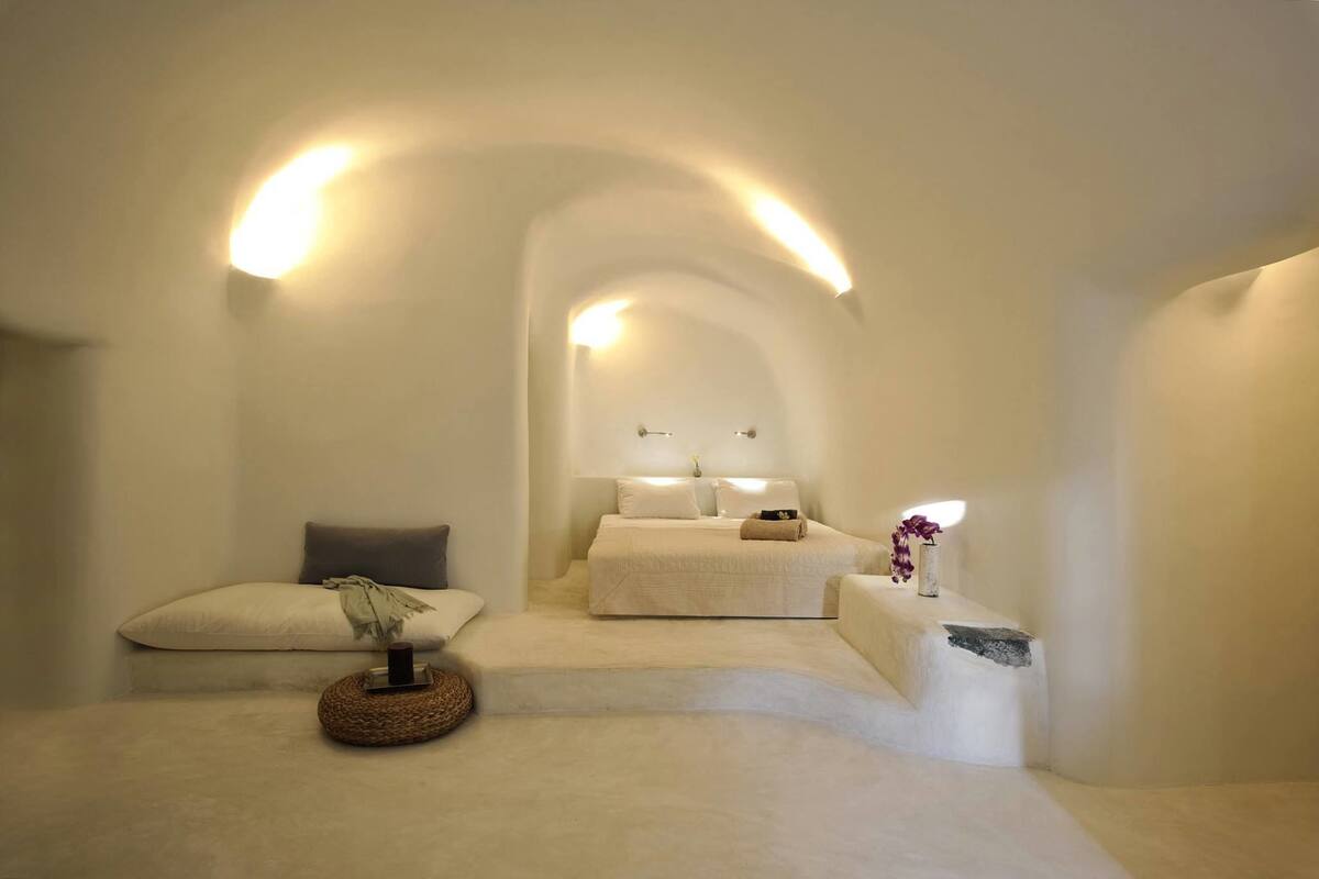 A minimalist bedroom with a bed, a bedside table, and a small seating area.