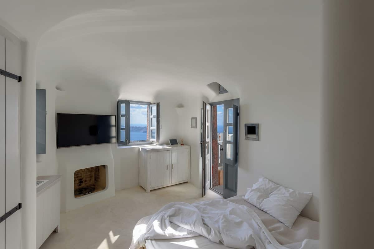 A bedroom with a bed, a desk, and a TV. There are windows and doors.
