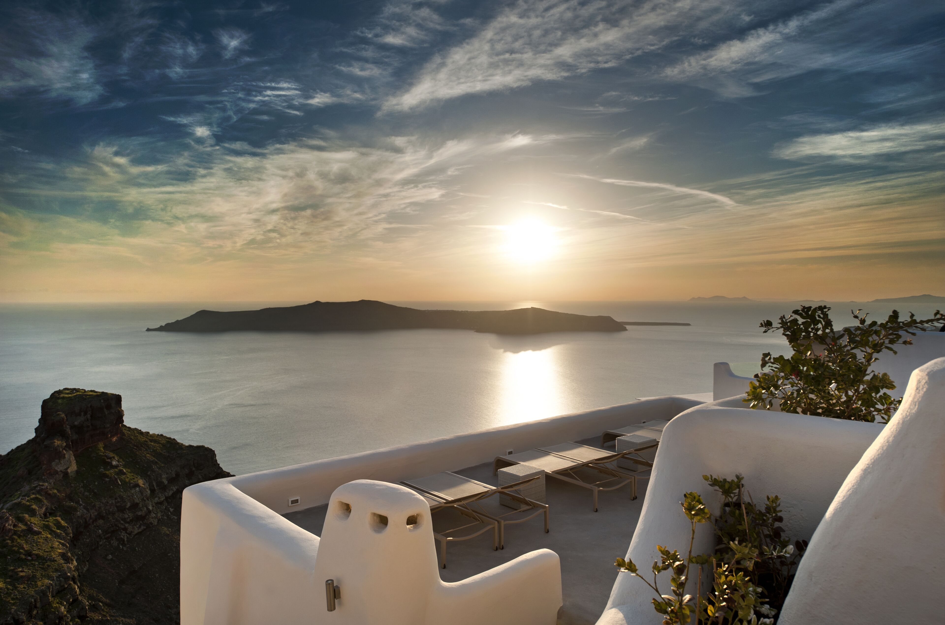 Une vue sur la mer avec un coucher de soleil, une architecture blanche et des chaises longues.
