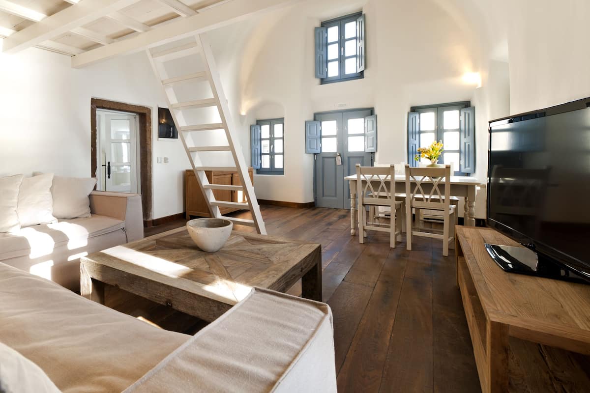 A spacious living area with a wooden floor, a sofa, a coffee table, a TV, and a dining area with a table and chairs.
