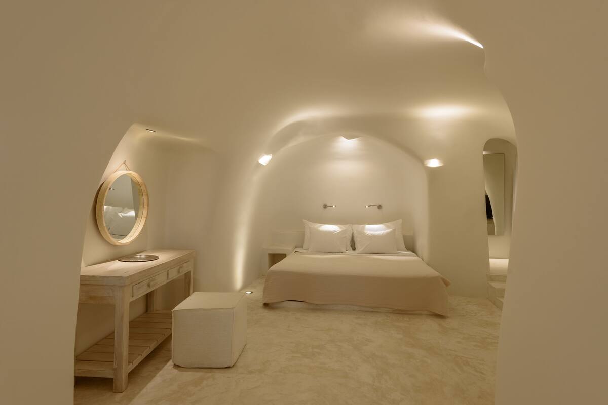 A bedroom with a bed, a vanity with a mirror, and a small stool.