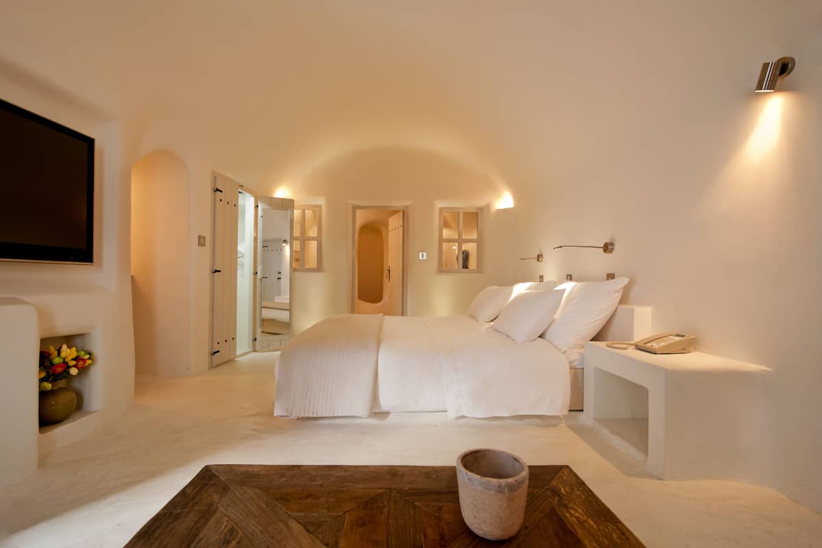 A spacious bedroom with a large bed, a bedside table with a lamp, and a flat-screen TV mounted on the wall.
