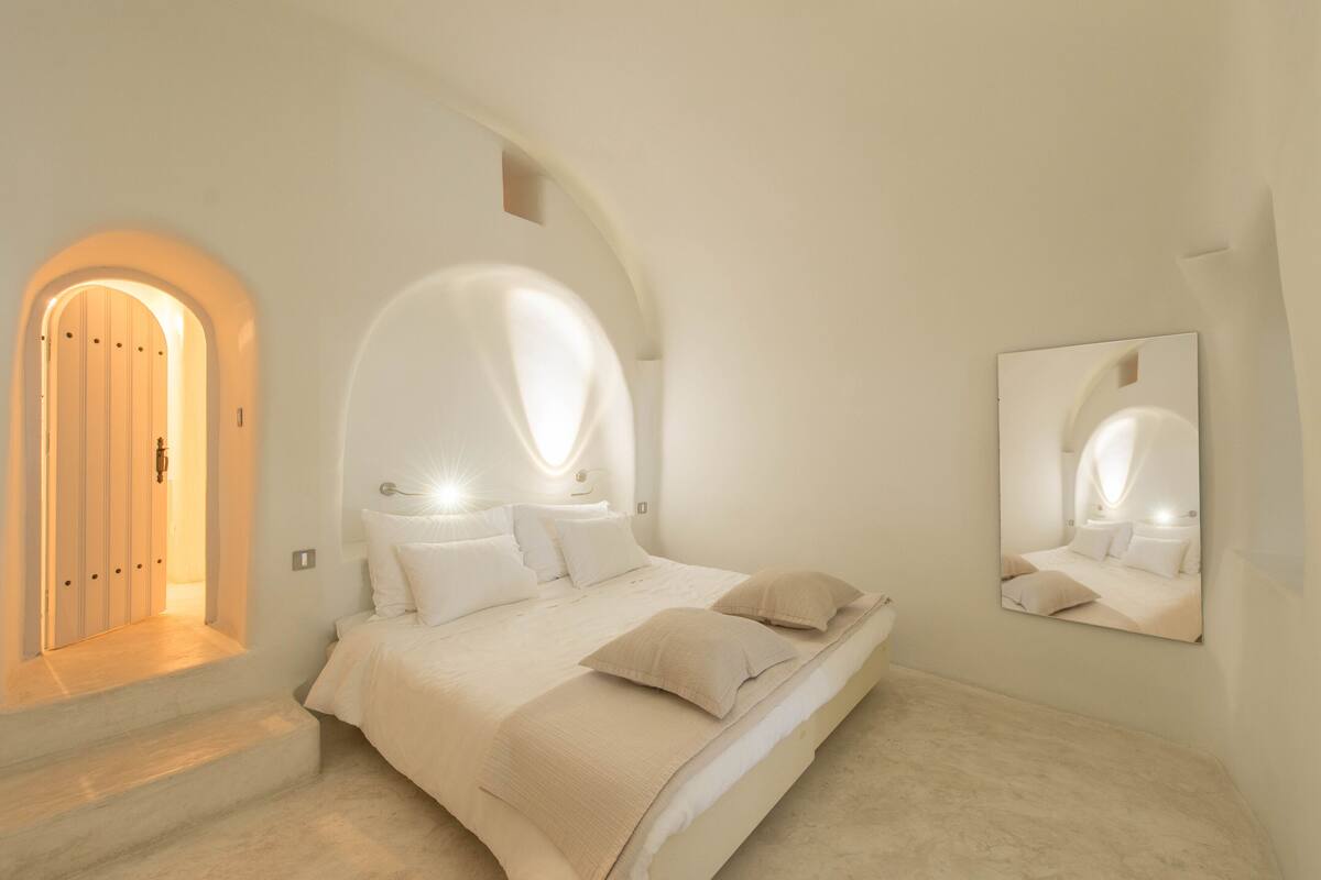 A bedroom with a large bed, an arched doorway, and a mirror on the wall.