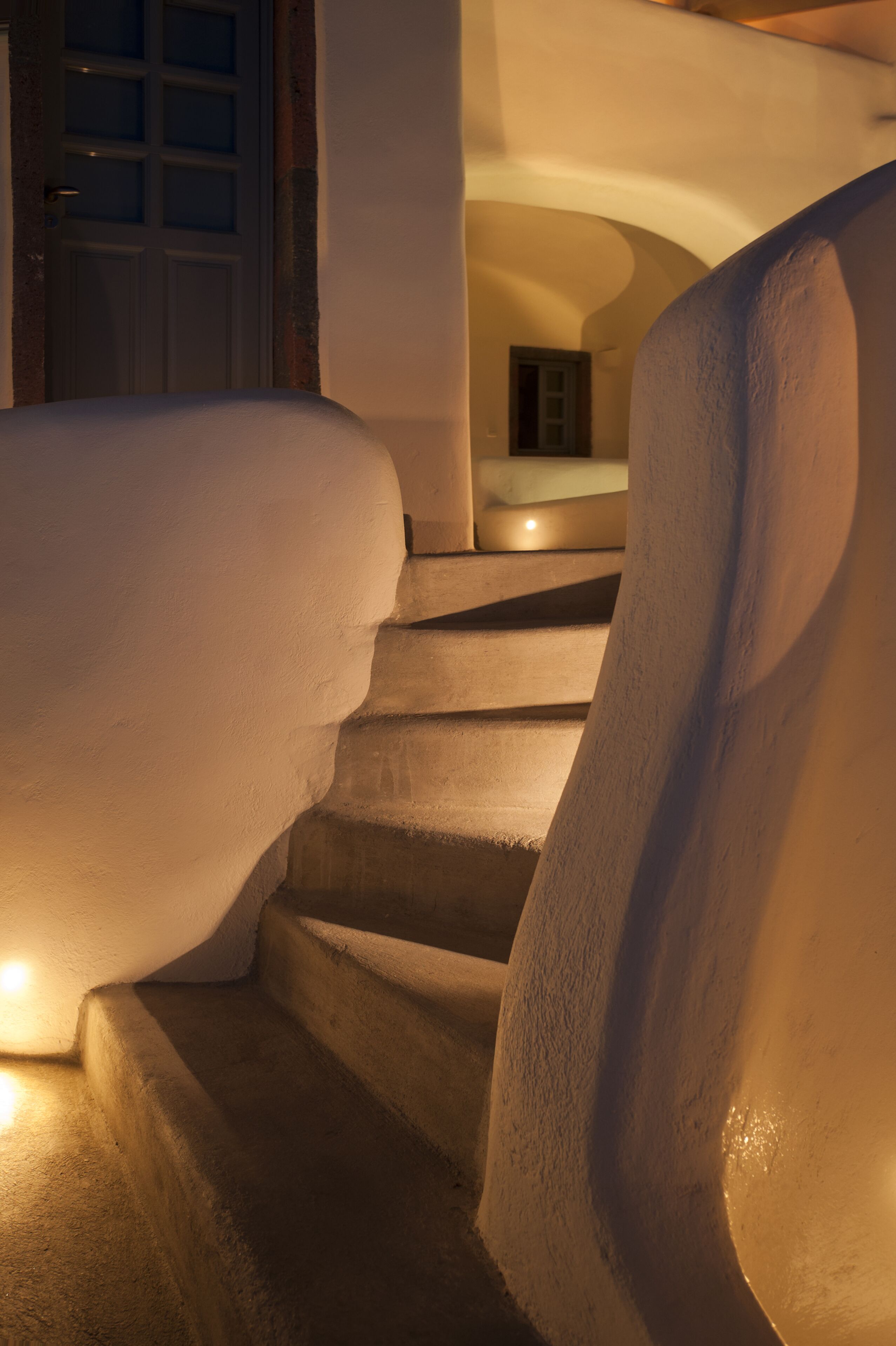 A staircase with a unique architectural design, featuring curved walls and a warm light source at the bottom.