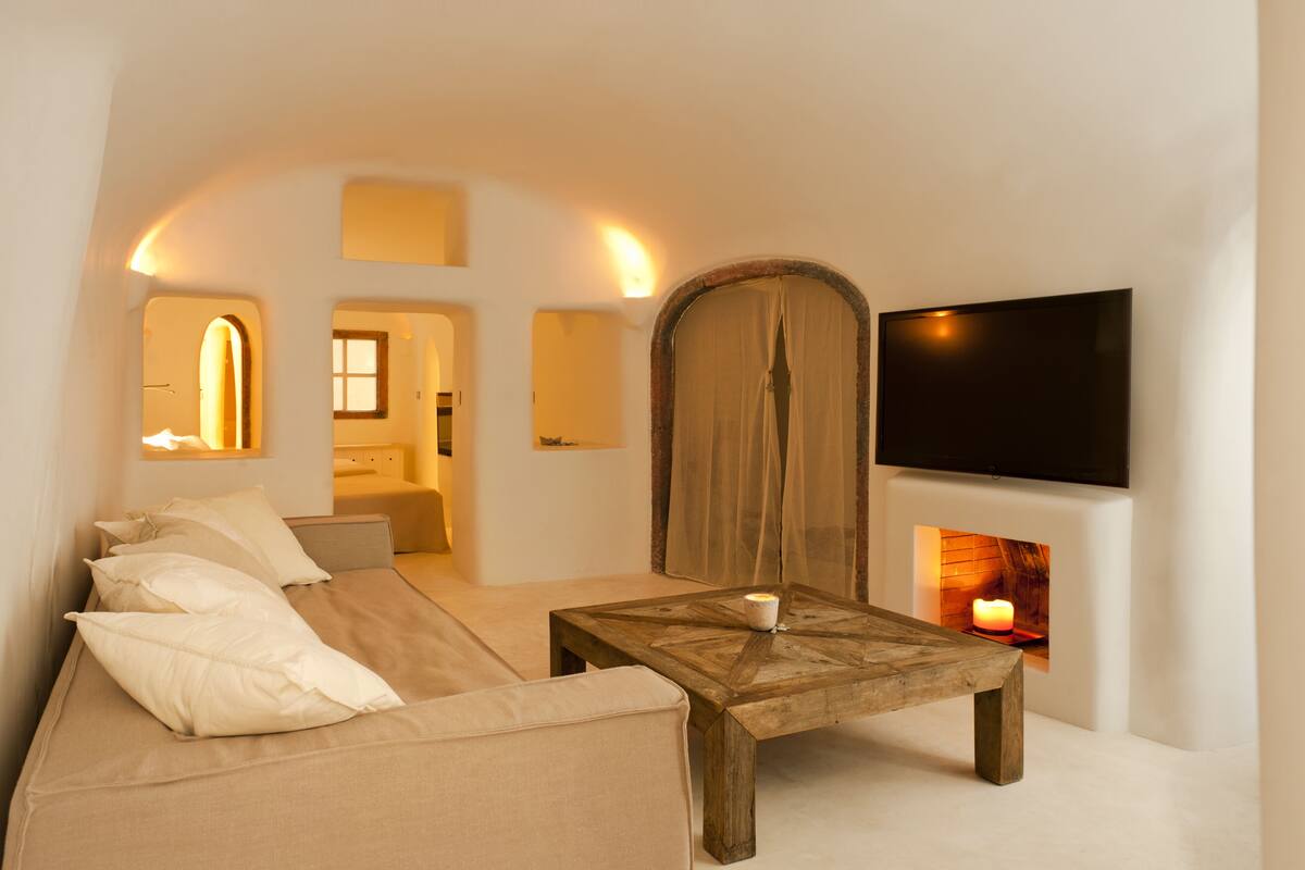 A modern, minimalist living room with a sofa, a wooden coffee table, a TV, and a fireplace.