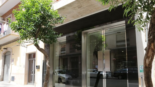 A modern building with large glass doors, a tree in front, and a parked car inside. - Hotel Europa (Foggia)