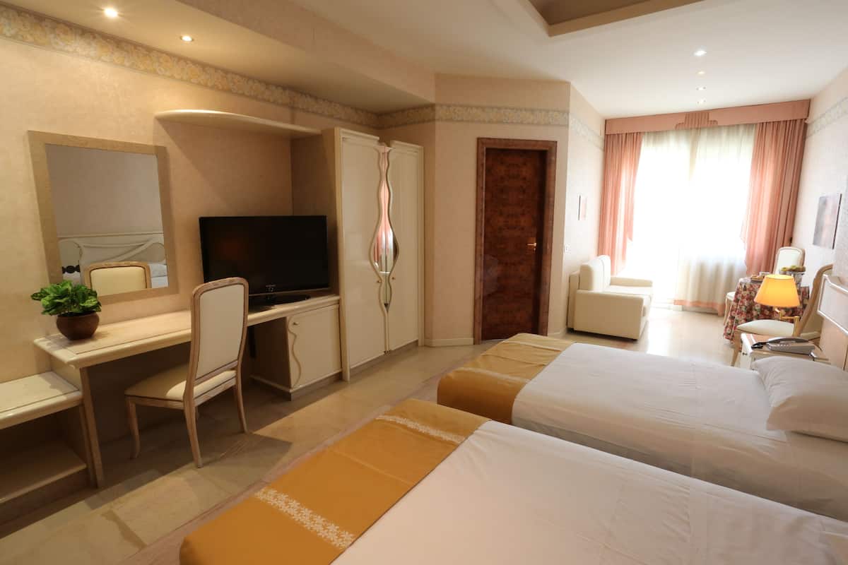 Ein Hotelzimmer mit Bett, Schreibtisch, Fernseher, Sessel, Kleiderschrank und einem Fenster mit Vorhängen.