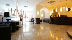 A modern hotel lobby with a reception desk, seating area, and a large mirror. - Hotel Europa (Foggia)