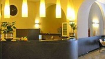 A reception area with a curved desk, multiple pendant lights, a clock, and potted plants.