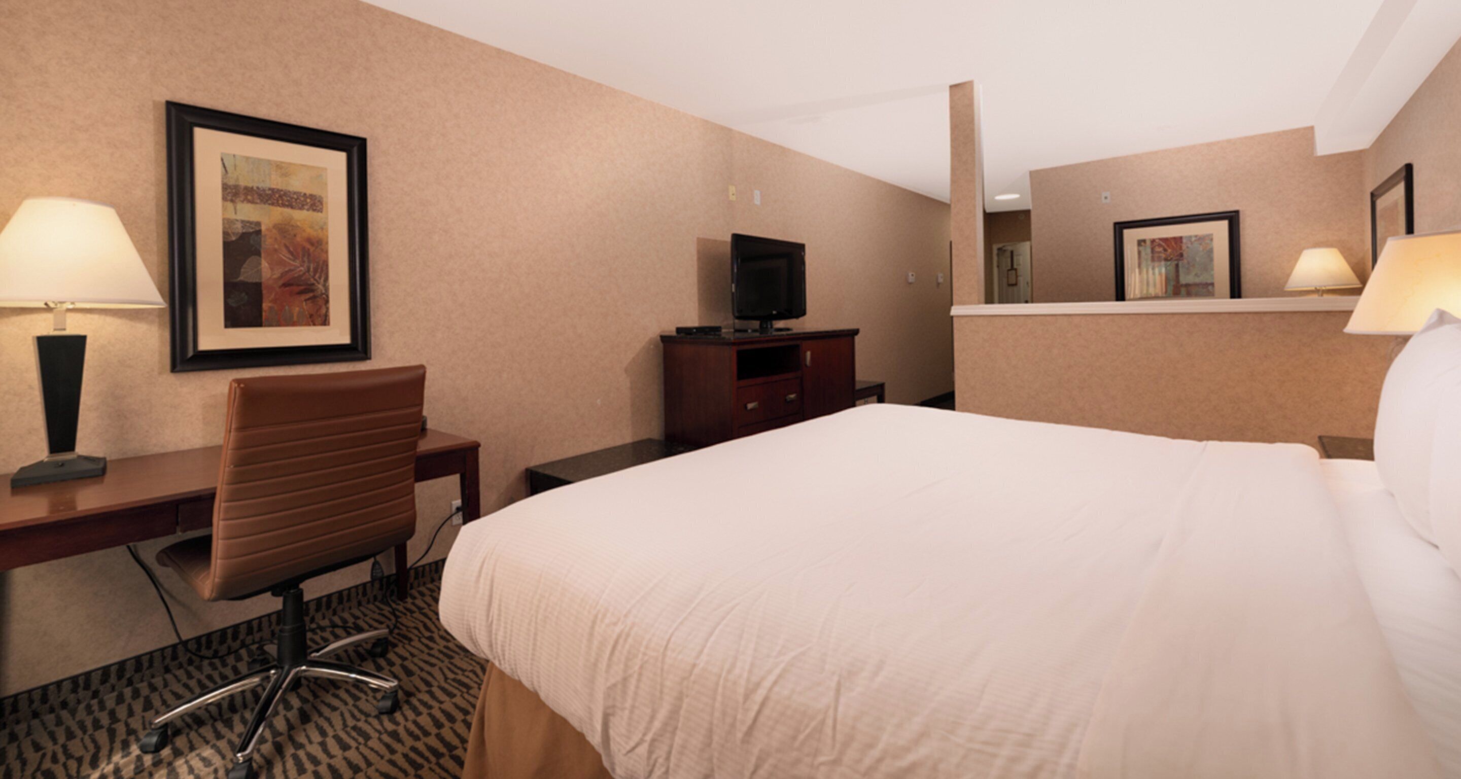 A hotel room with a bed, desk, chair, television, and lamps.
