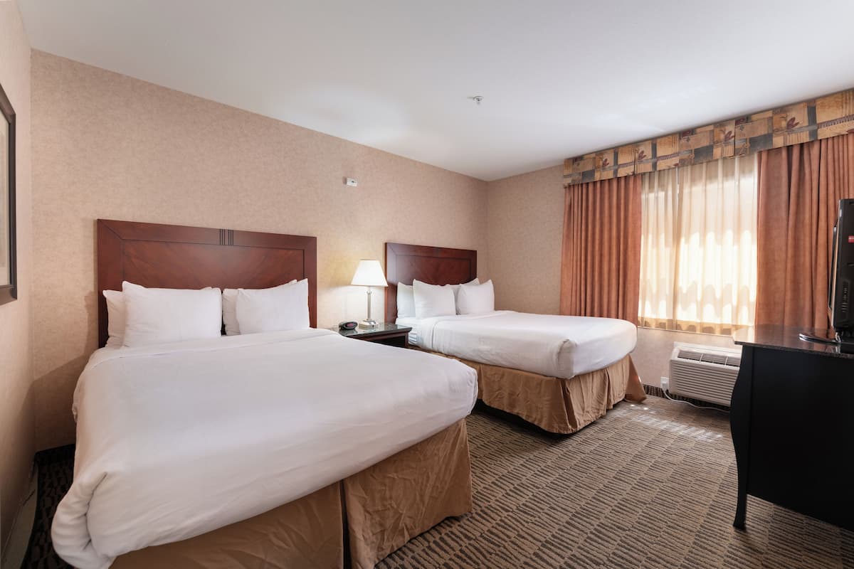 A hotel room with two beds, a desk, a lamp, and an air conditioning unit.