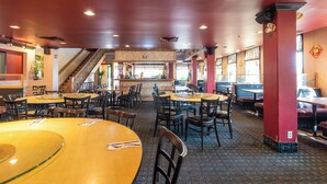 A spacious restaurant with multiple dining tables and chairs, a staircase leading to an upper level, and a view of the street outside.
