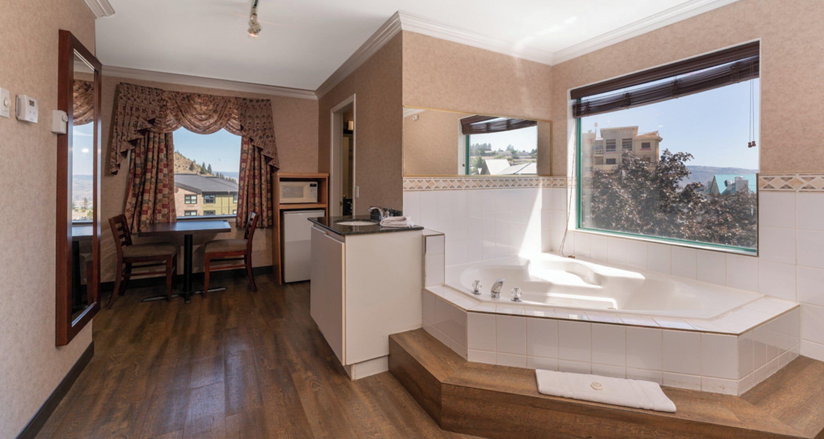 A modern bathroom with a large bathtub, a shower, and a vanity. There is a window with a view of buildings and trees.