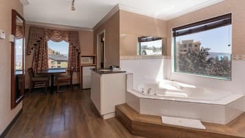 A modern bathroom with a large bathtub, a shower, and a vanity. There is a window with a view of buildings and trees.