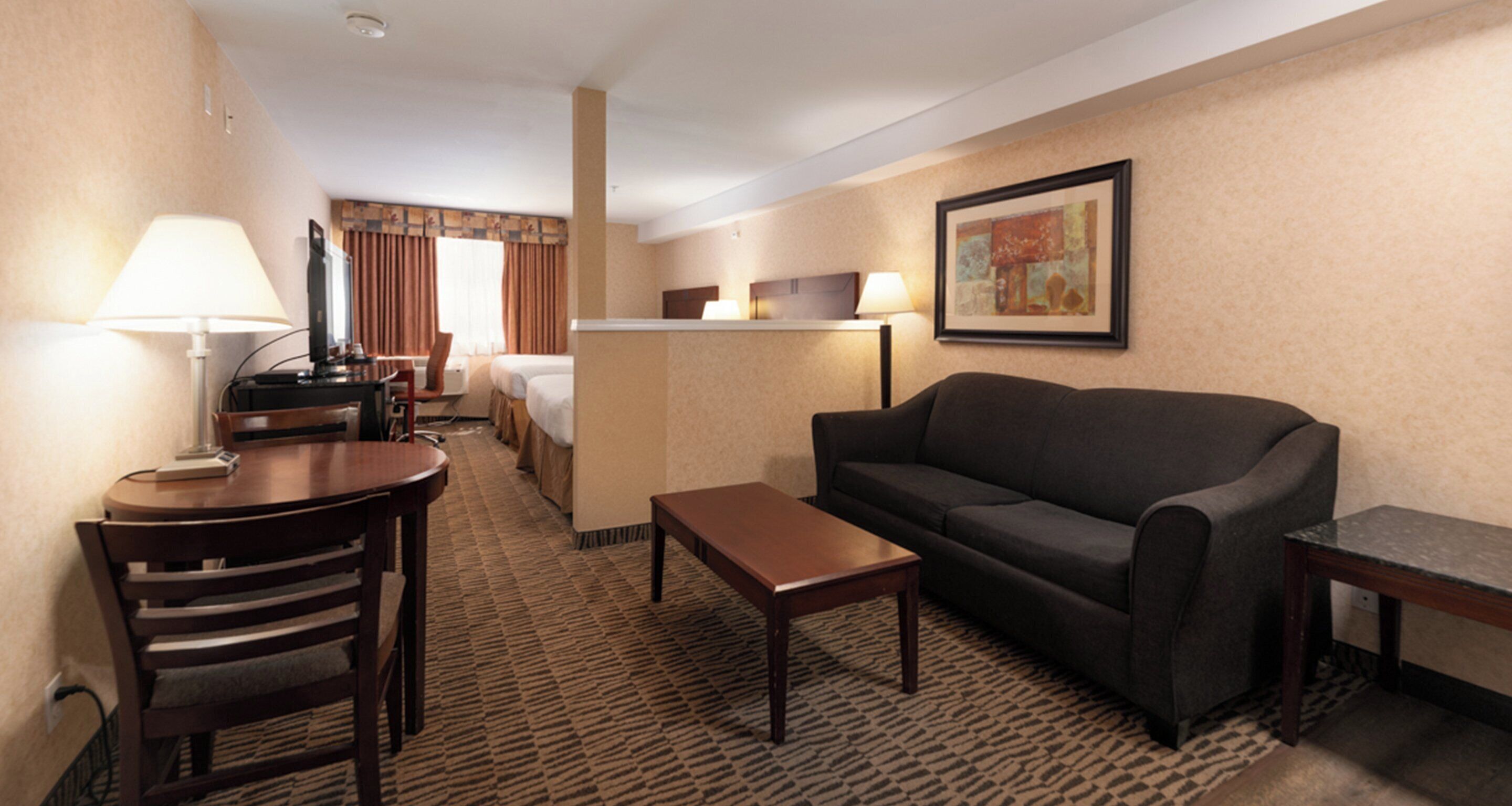 Ein Hotelzimmer mit einer Couch, einem kleinen Tisch, einer Lampe, einem Fernseher und einem Bett.