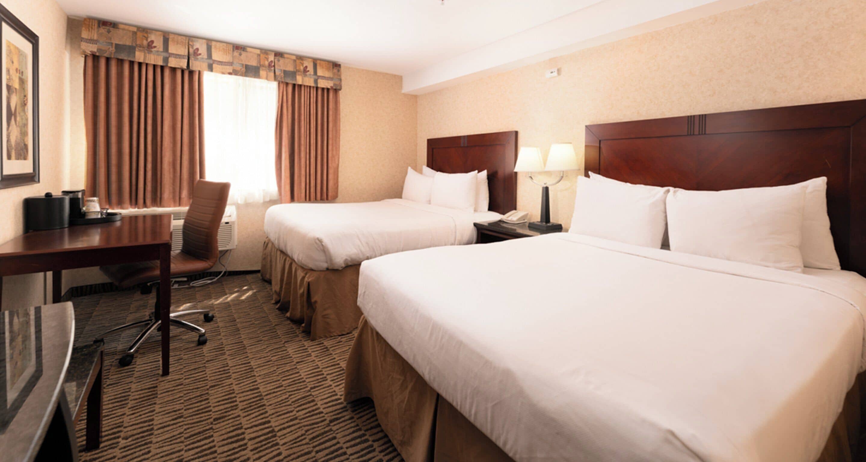A hotel room with two beds, a desk with a chair, a lamp, and a telephone.