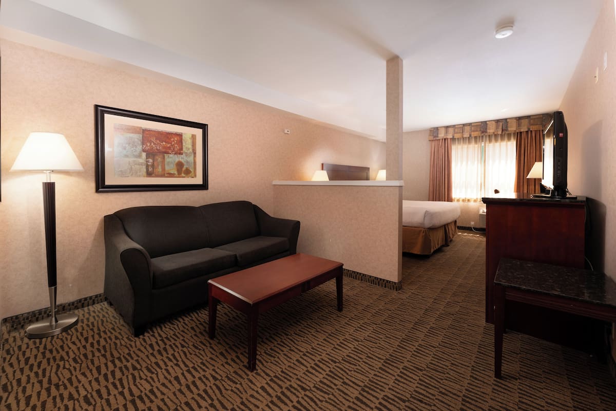 A hotel room with a sofa, a small table, a bed, a TV, and a lamp.