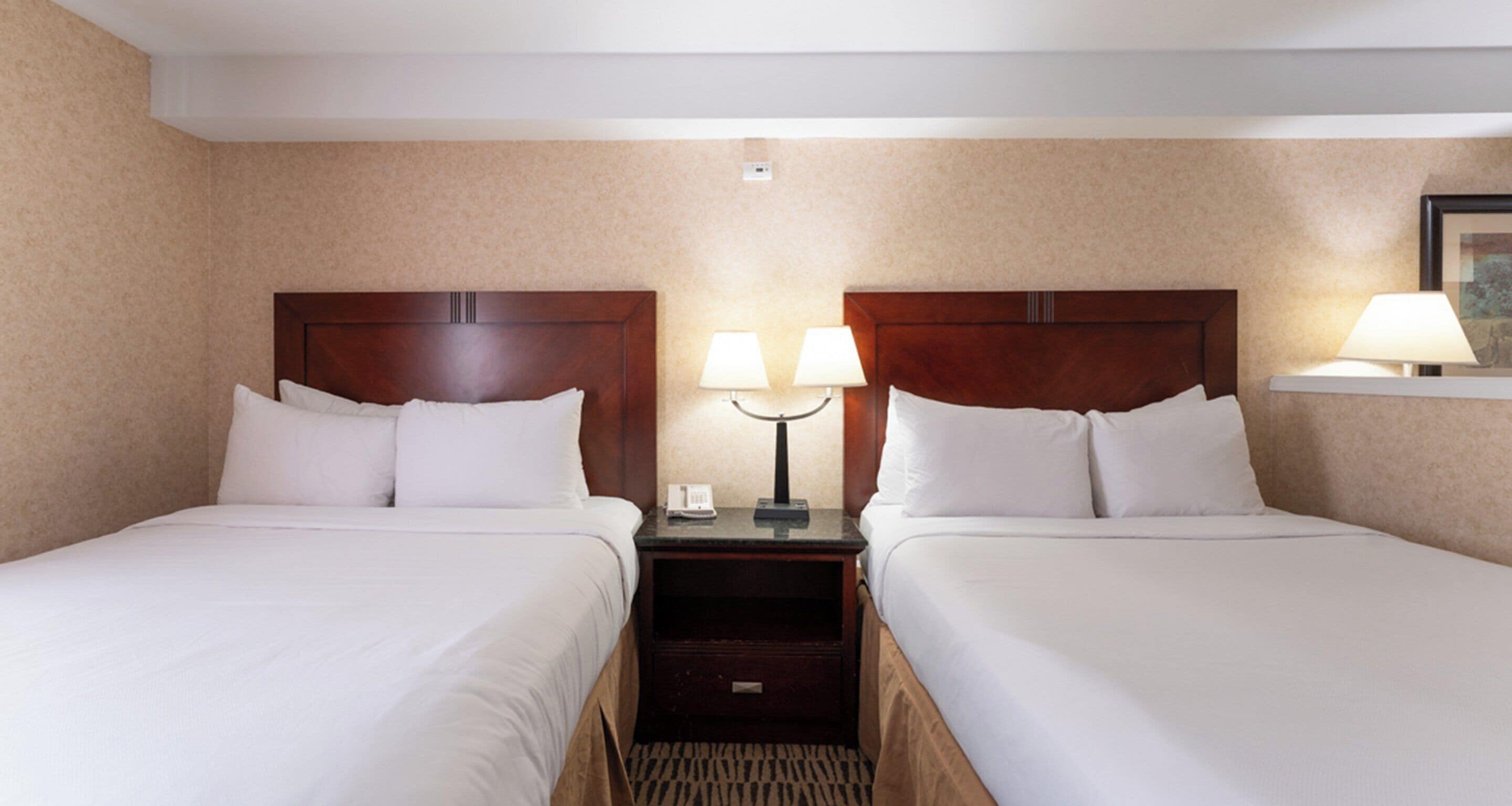 A hotel room with two single beds, a nightstand with a lamp, and a small drawer.