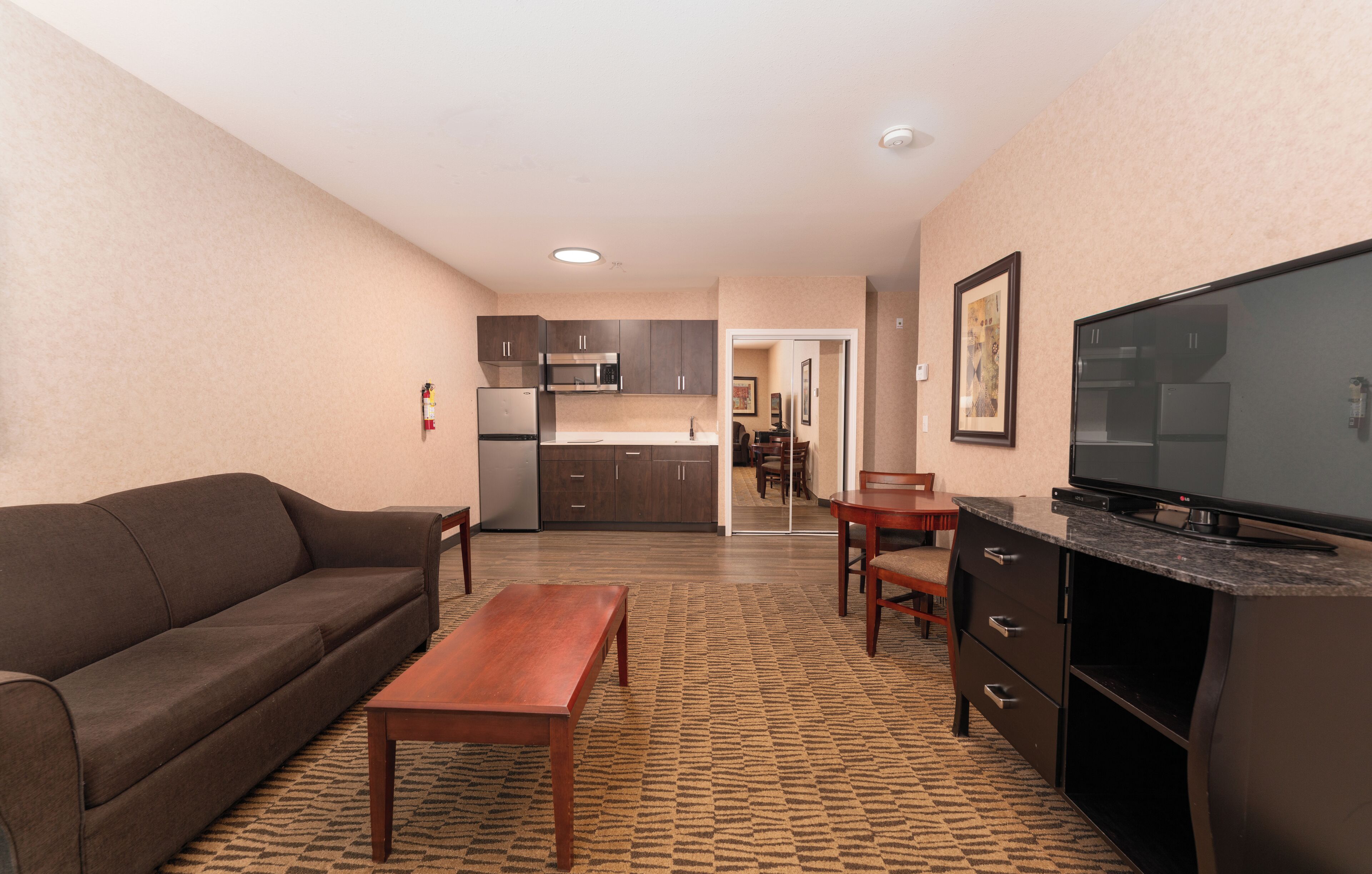 A compact living space with a sofa, a wooden table, a TV, a kitchen area, and a dining table.