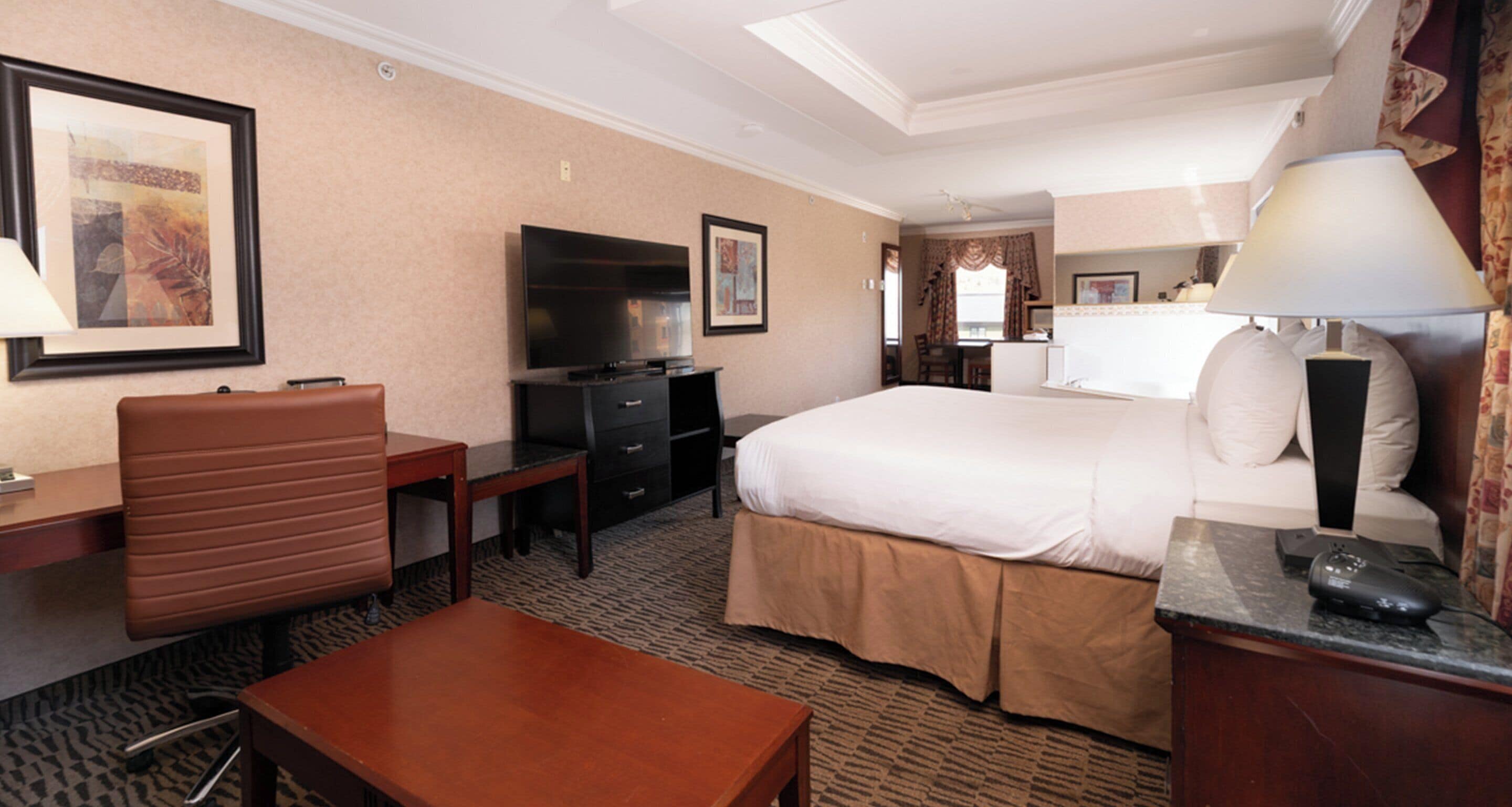 A hotel room with a bed, desk, chair, TV, and a small table.