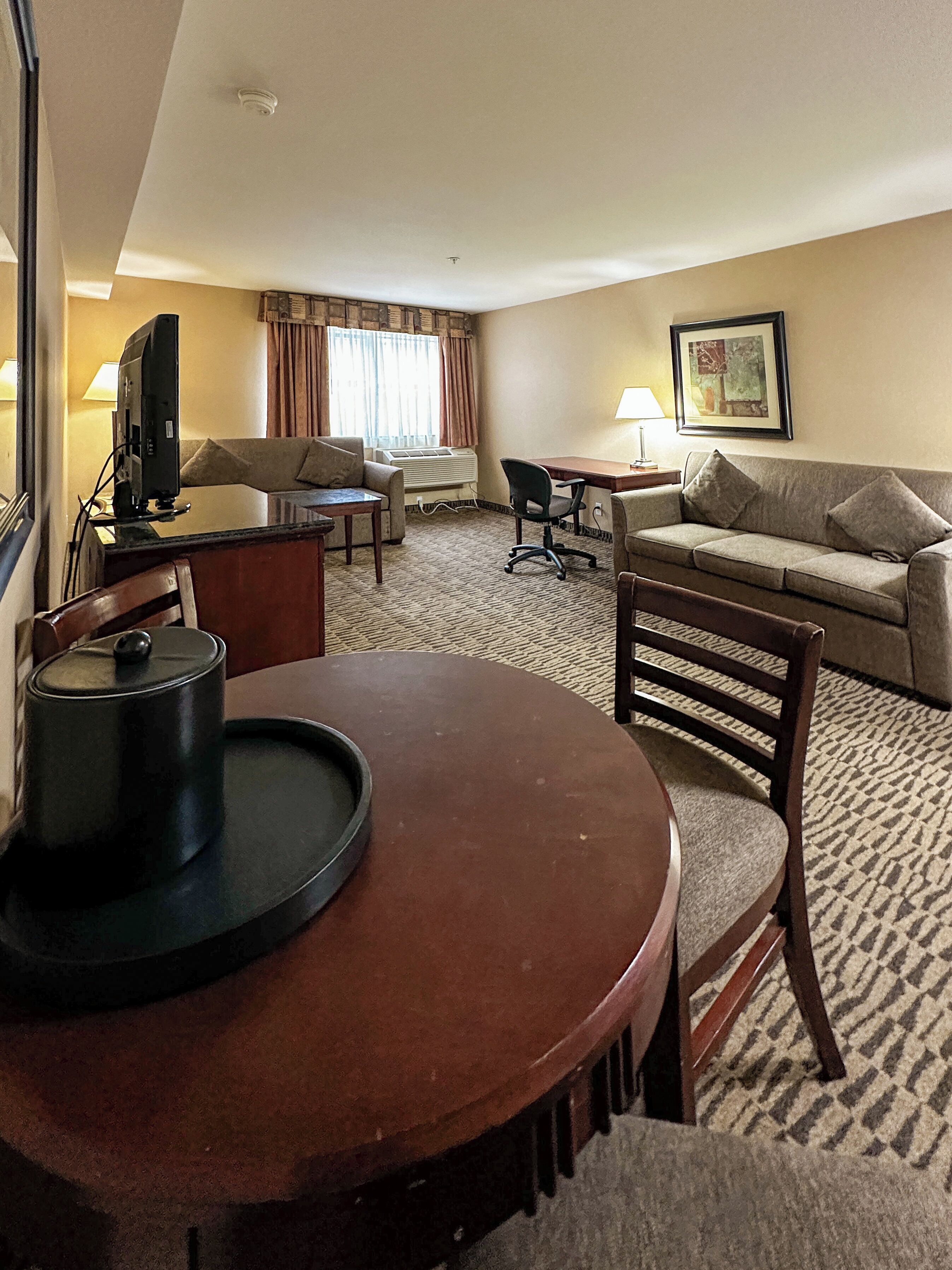 A hotel room with a round dining table, a sofa, a chair, a TV, and a framed picture on the wall.