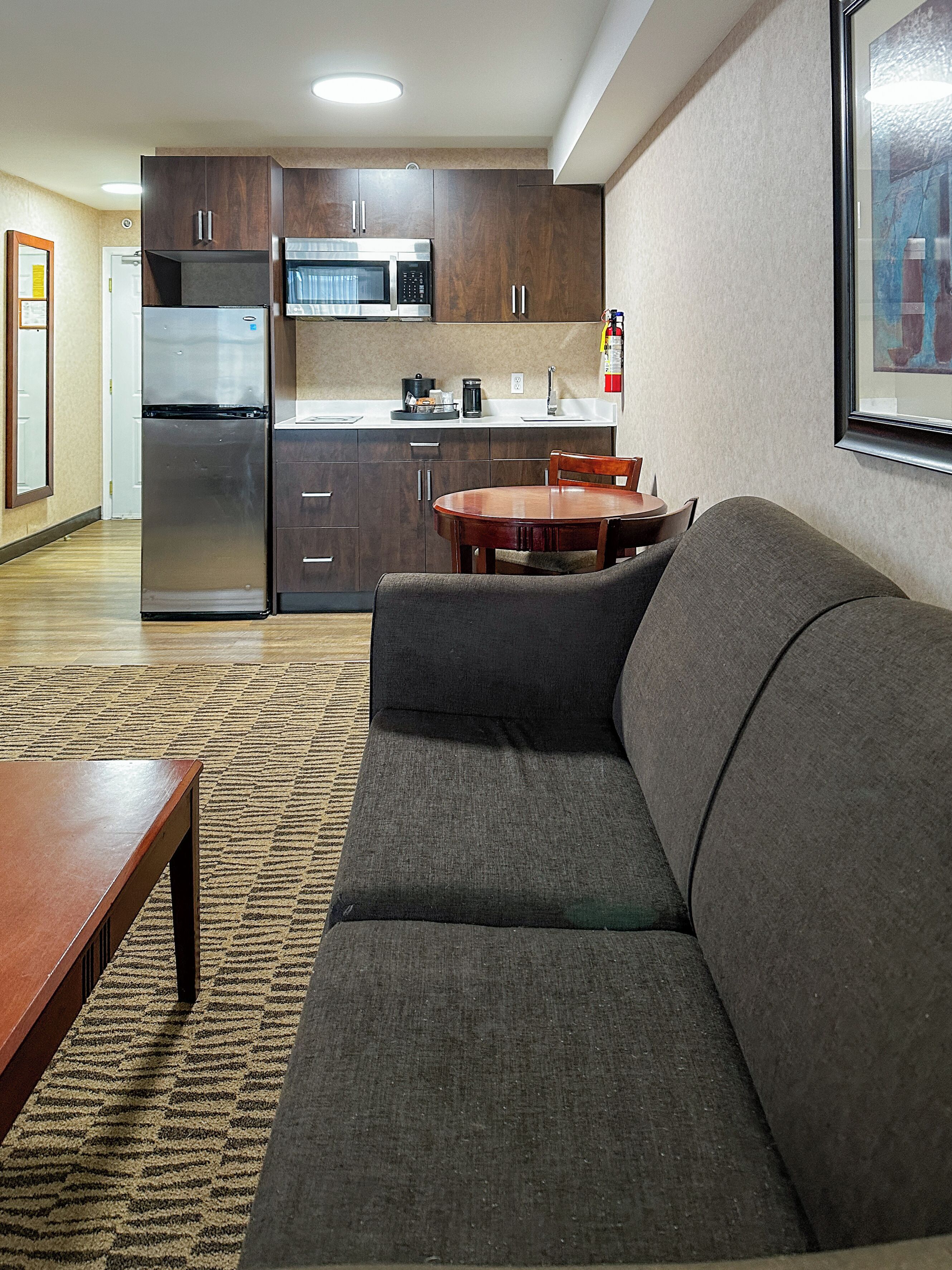 A modern kitchen with stainless steel appliances, a dining area with a wooden table and chairs, and a gray sofa in a living area.
