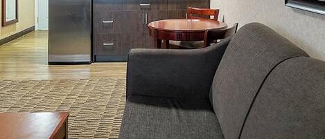 A modern kitchen with stainless steel appliances, a dining area with a wooden table and chairs, and a gray sofa in a living area.