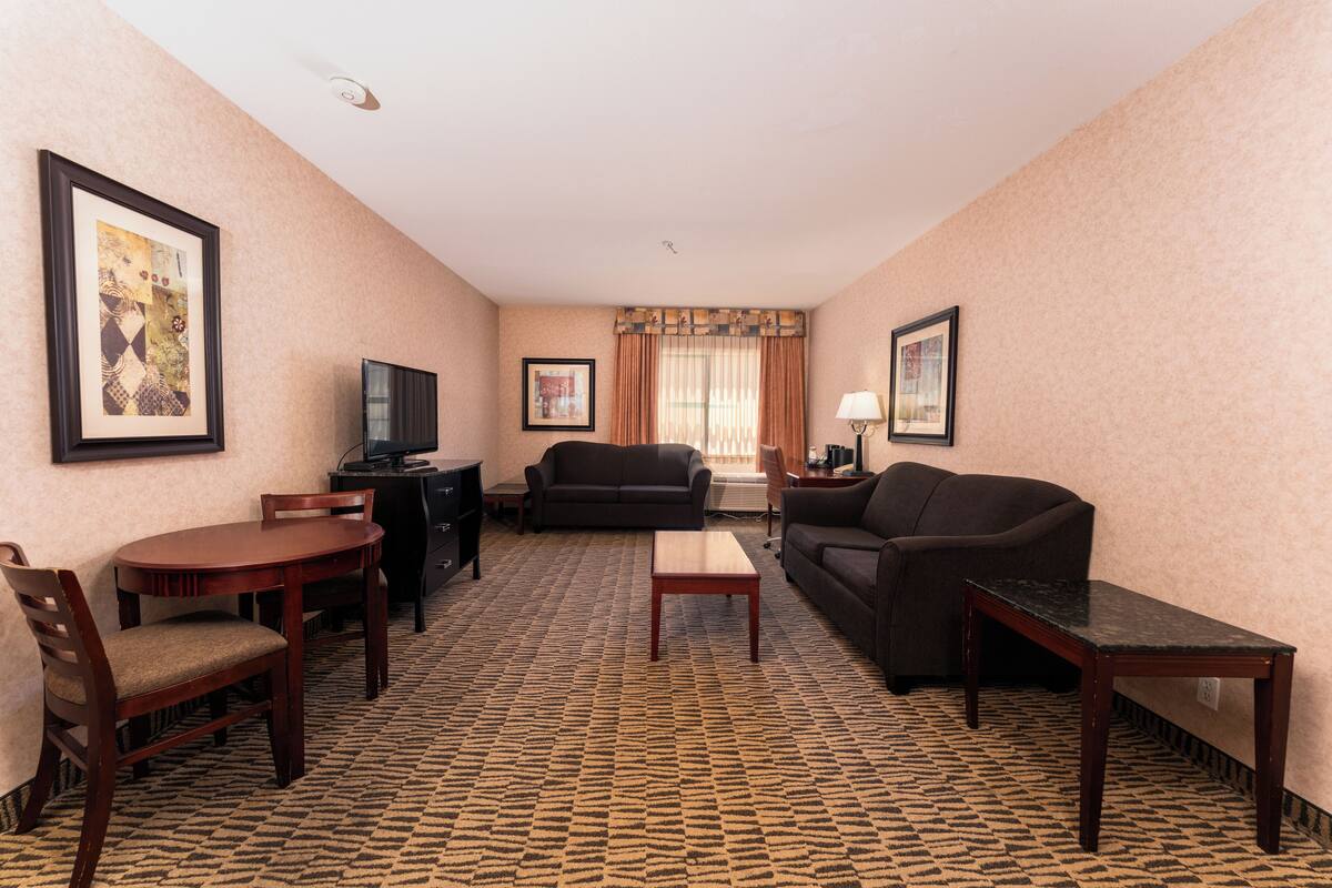 A hotel room with a dining table, two sofas, a TV, and a patterned carpet.