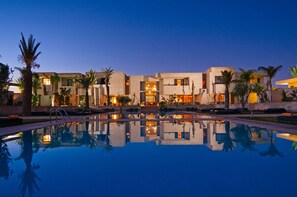 A modern hotel with a pool, palm trees, and a clear night sky.