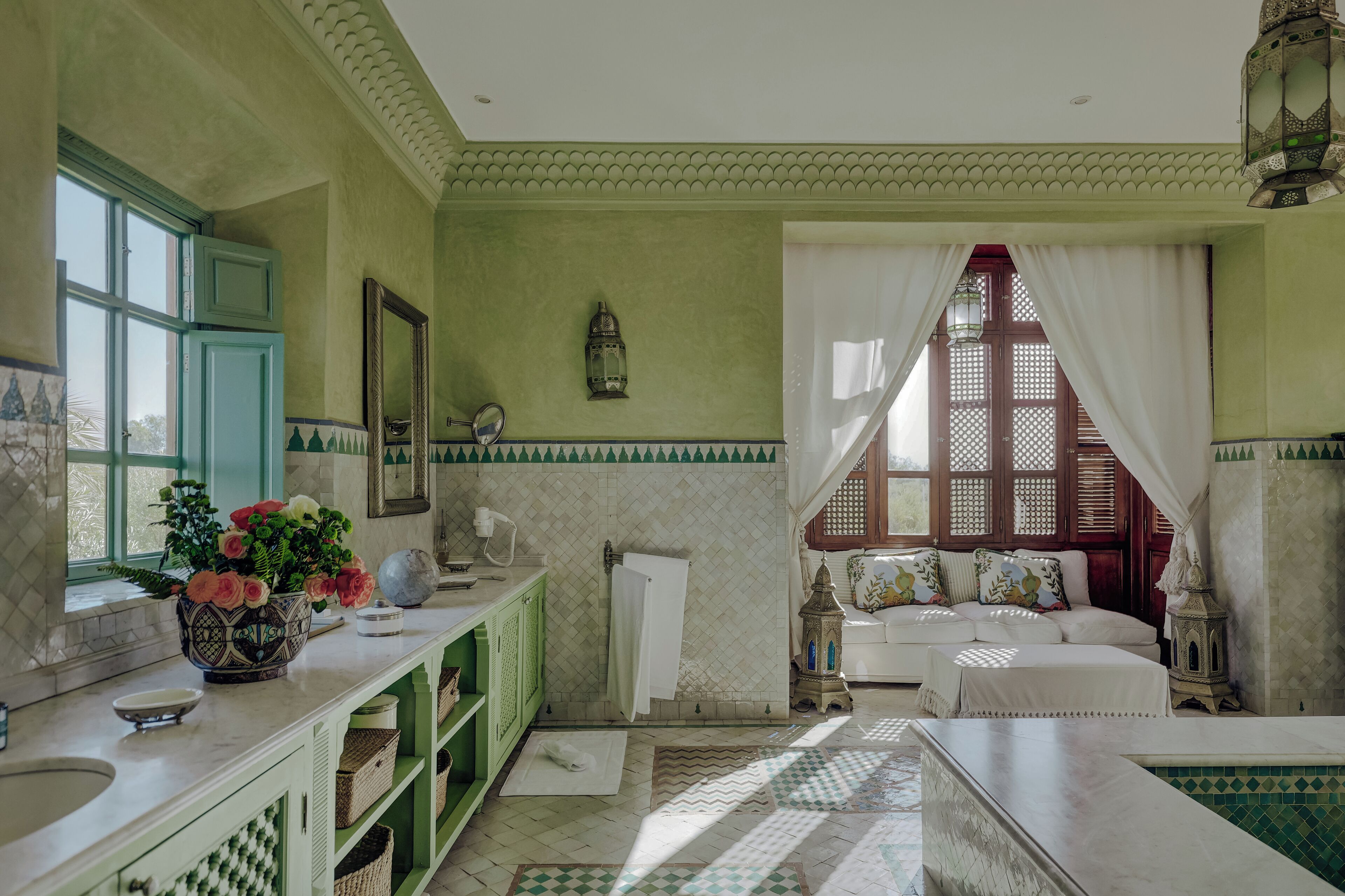 A room with a green and white tiled floor, a white sofa, a green cabinet, a window with white curtains, and a decorative lantern.