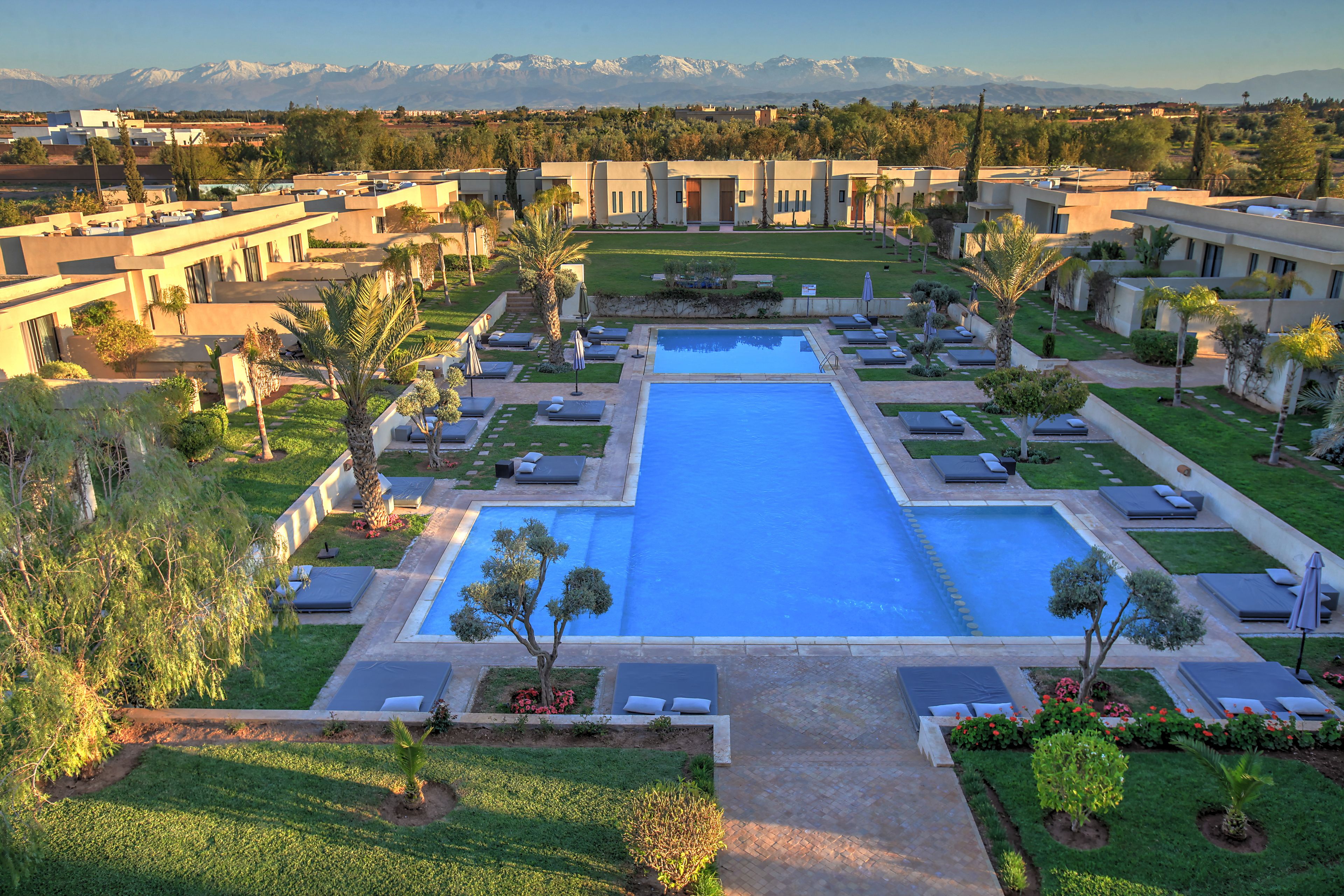 Un resort con una piscina centrale, diverse zone relax e vista sulle montagne lontane.