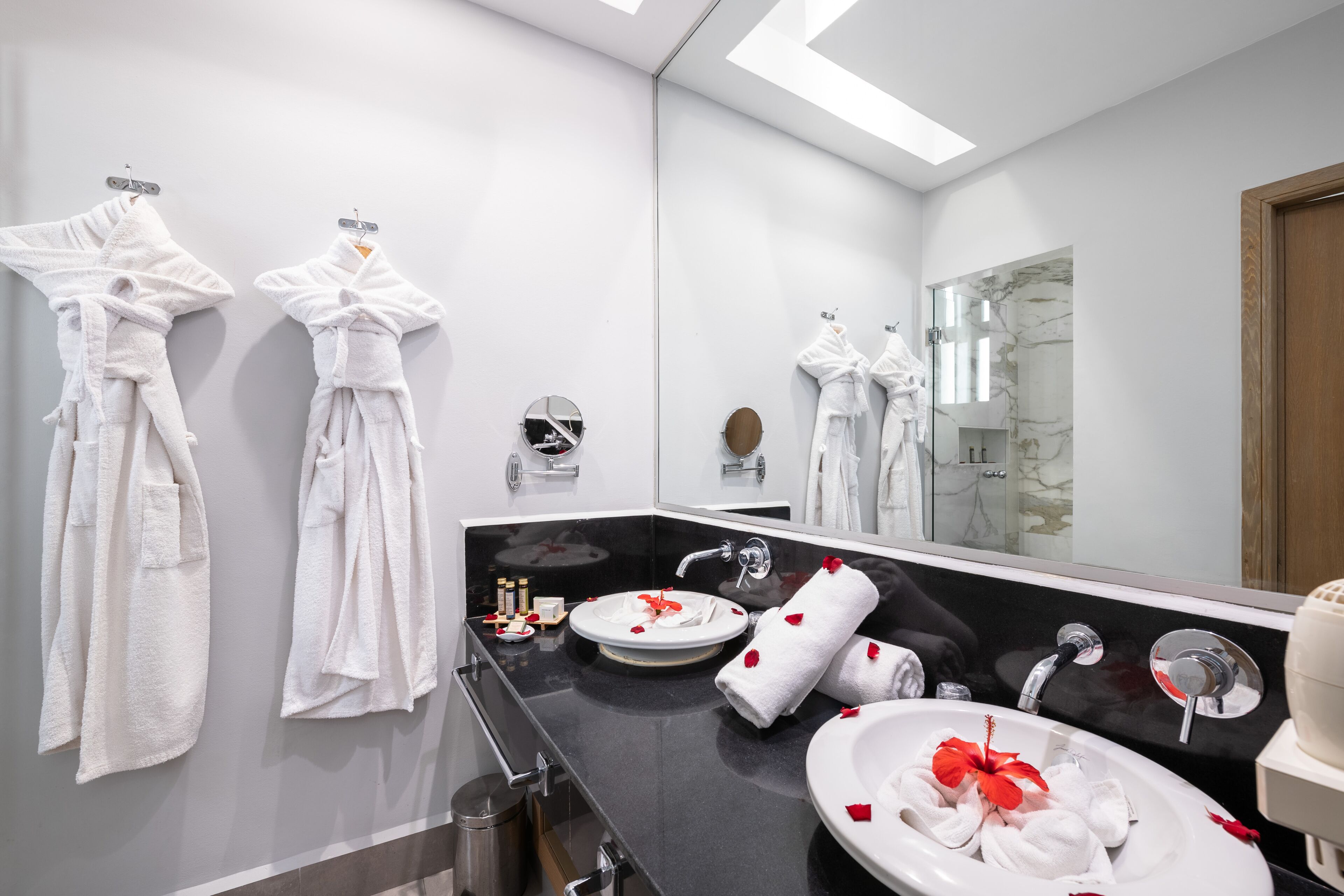A modern bathroom with two white towels hanging on hooks, a round mirror, a black countertop, and a sink with a white basin.