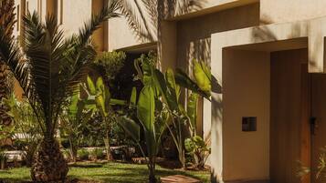 A courtyard with palm trees and a building with a beige facade and rectangular windows.