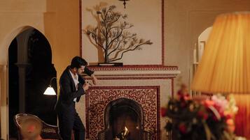A man in a suit standing by a fireplace with a decorative tree sculpture above it.