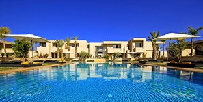 A swimming pool with lounge chairs and umbrellas, surrounded by buildings with a modern architectural style.