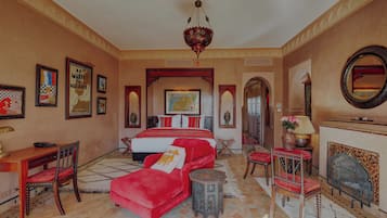 Un dormitorio espacioso con una cama grande, un sofá rojo, un escritorio de madera y una chimenea.