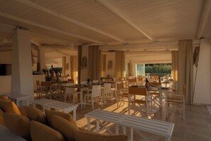 A spacious indoor area with multiple dining tables and chairs, a sofa, and a view of greenery outside. - Ostuni a Mare (Ostuni)