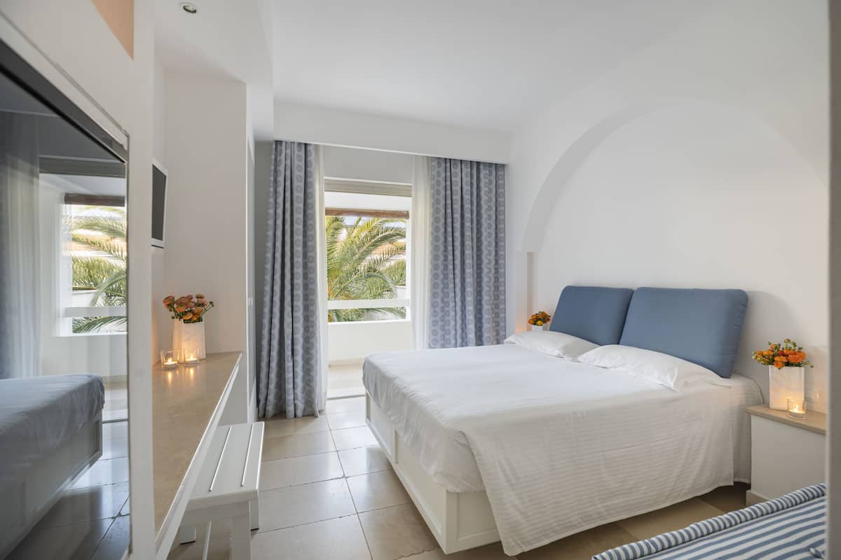 A modern hotel room with a large bed, a small seating area, and a balcony with curtains.