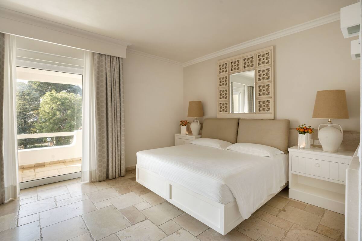 A bedroom with a large bed, a nightstand, a dresser, a mirror, and a window with curtains.
