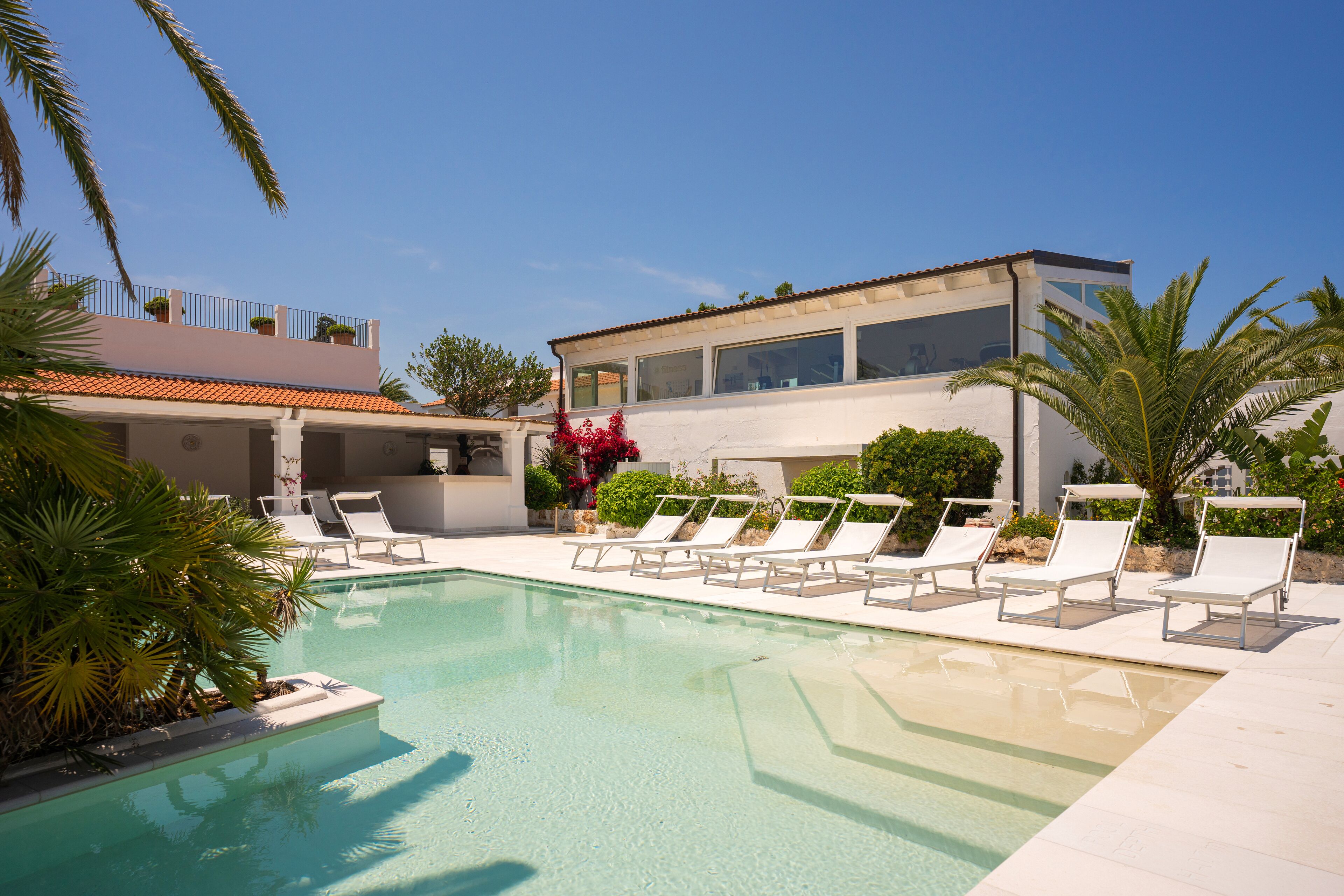 A swimming pool with lounge chairs, a modern building, and palm trees.