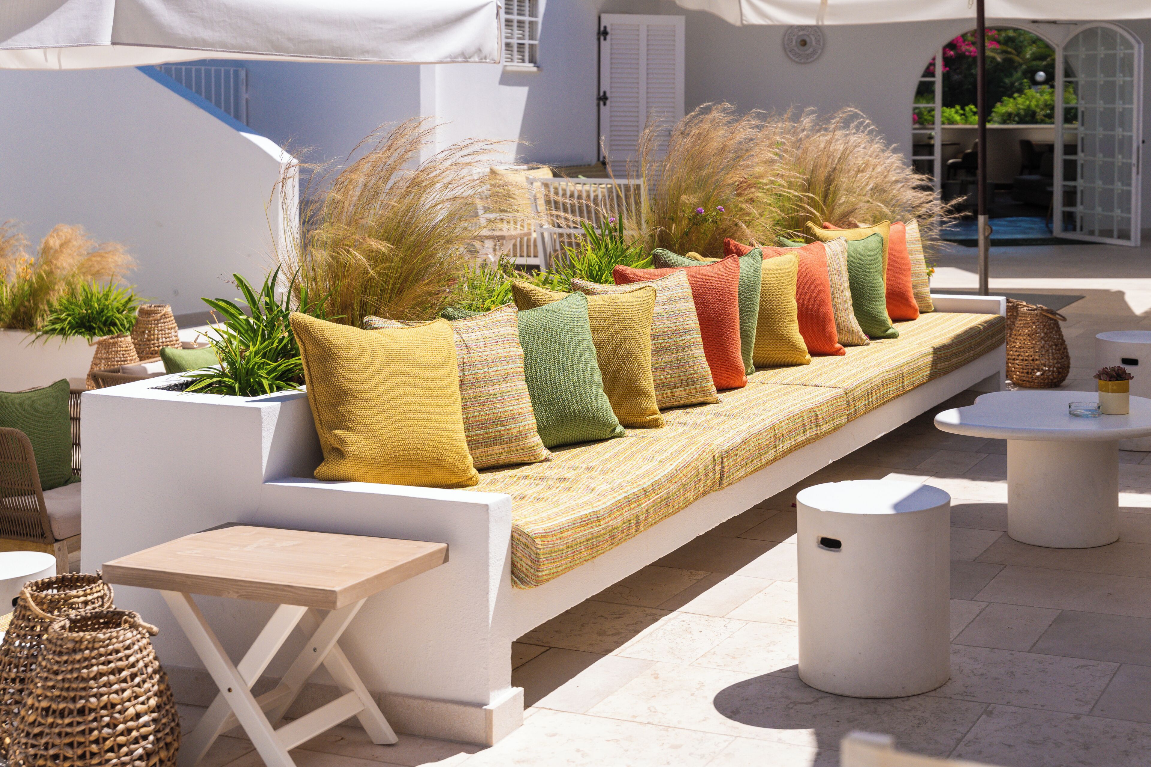 Un espace extérieur aménagé avec des sièges blancs, des coussins, une petite table et un panier.