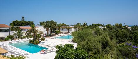 A resort with a large swimming pool, sun loungers, and lush greenery.