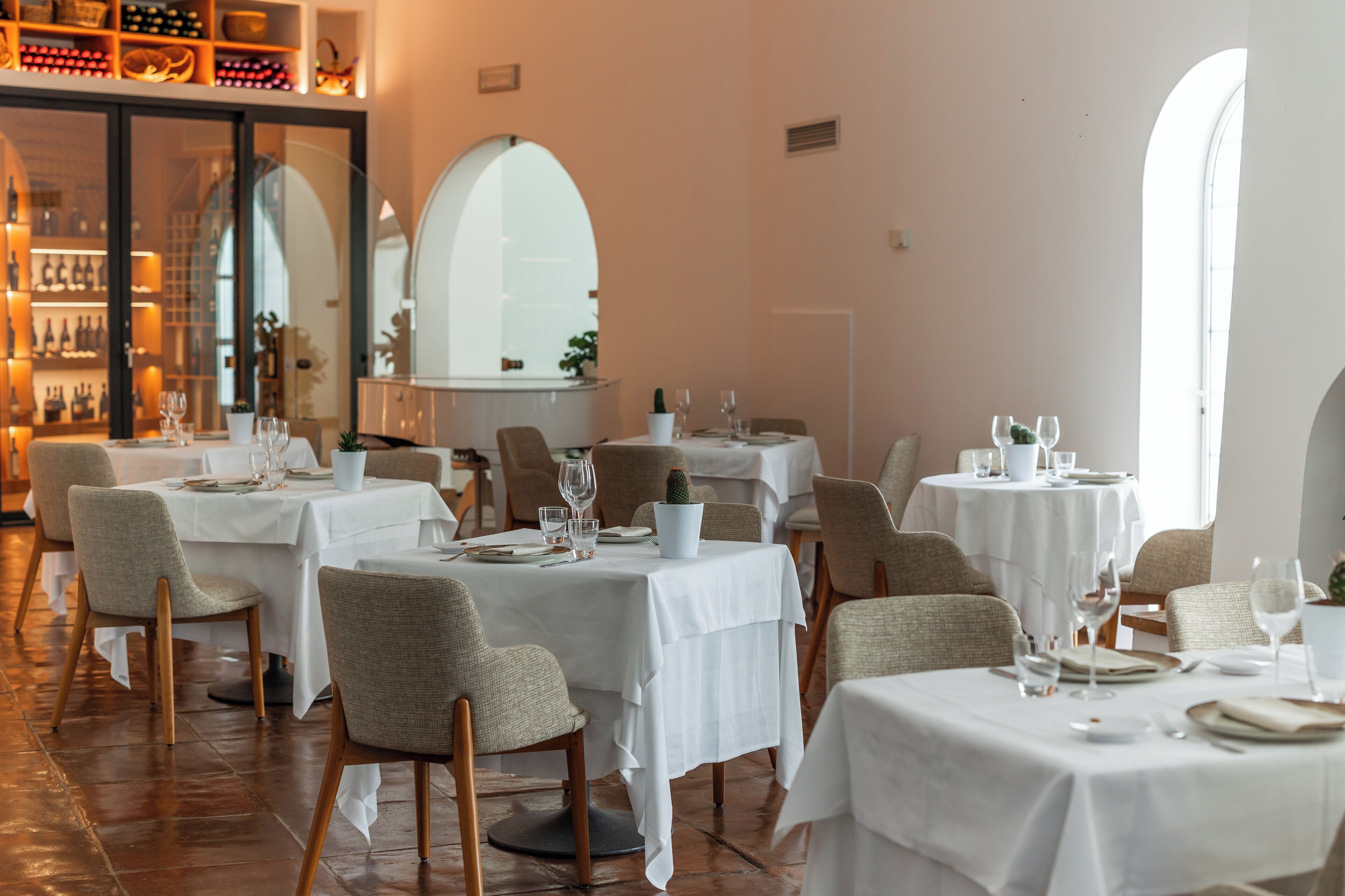 A restaurant with tables set for dining, chairs, and a wine rack in the background.